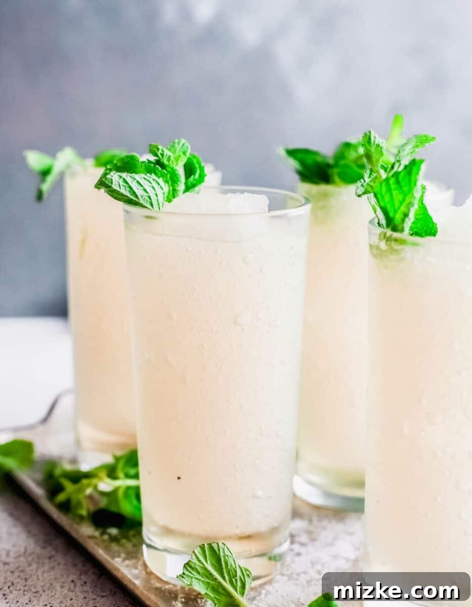 Minted Bourbon Frost 2 Four perfectly blended frozen mint juleps are placed on a sophisticated serving tray, garnished with vibrant fresh mint sprigs, ready to be enjoyed.
