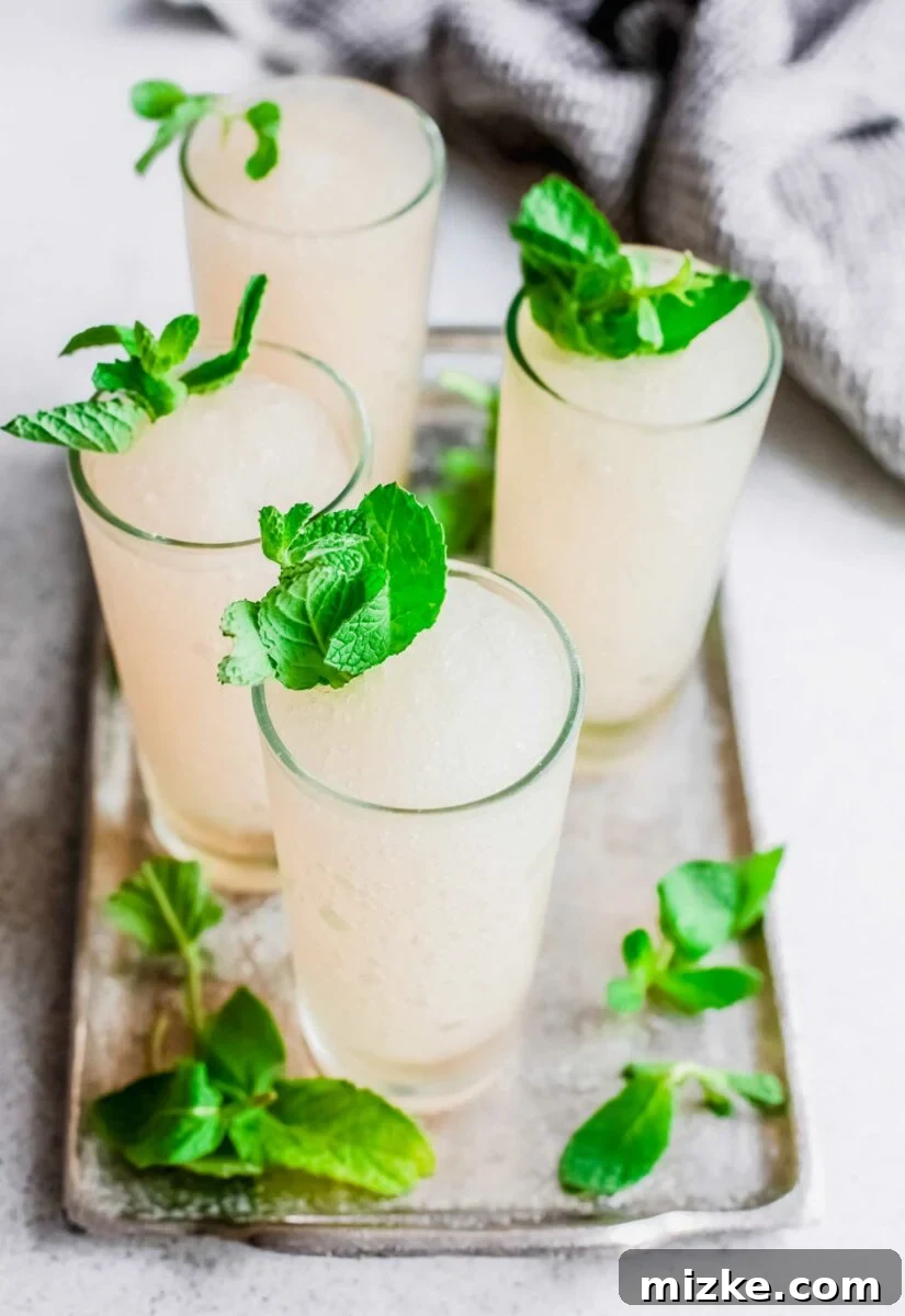 Minted Bourbon Frost 3 Fresh mint sprigs are delicately placed on and around four vibrant green frozen mint juleps, enhancing their visual appeal and inviting aroma.