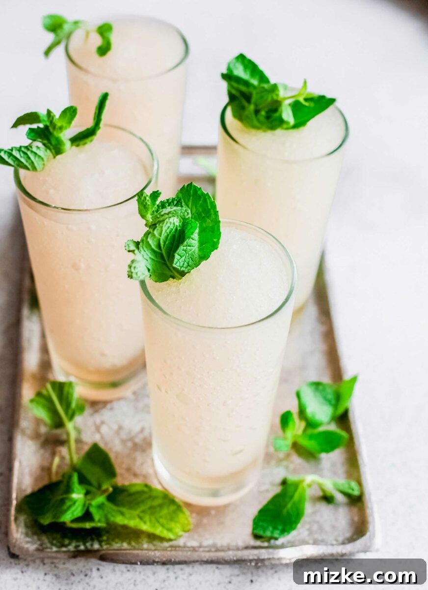 Minted Bourbon Frost 5 Lush green mint sprigs artfully adorn the tops of vibrant frozen cocktails, sitting elegantly in stylish glasses, ready for serving and enjoyment.