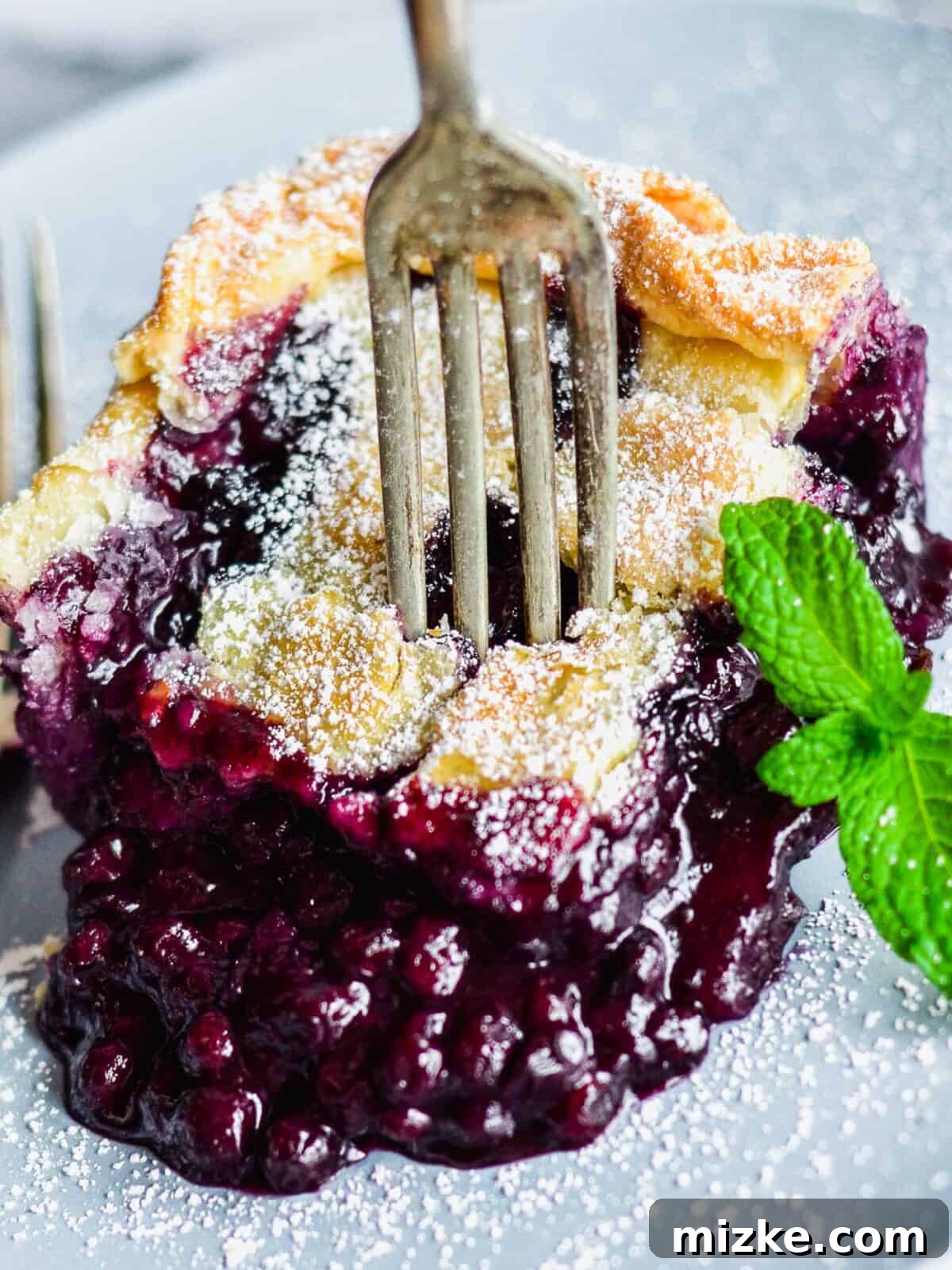 Mile High Wild Blueberry Pie 3 A fork piercing into a delicious slice of deep dish wild blueberry pie, showcasing the thick layer of juicy, glistening blueberries and the beautifully flaky crust.