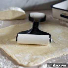 A baker flattening out pie crust dough with a rolling pin on a well-floured surface, preparing it for the baking dish.