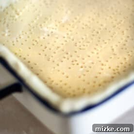 The bottom of the pie crust in the baking dish with fork pricks visible, ready for blind baking to prevent a soggy bottom.