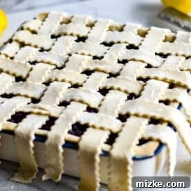 Pastry dough strips intricately woven into a classic lattice design over the wild blueberry filling in the baking dish, ready for the oven.