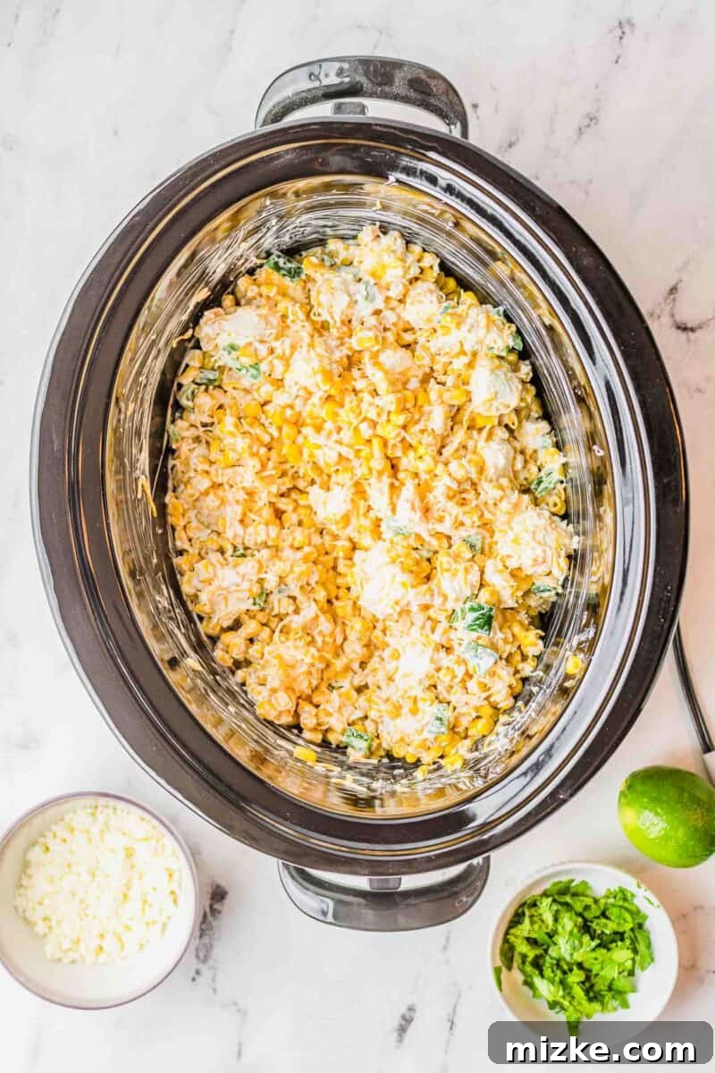 Ingredients for jalapeno corn dip, including corn, jalapeños, and various cheeses, are stirred together in the insert of a slow cooker to combine before cooking.