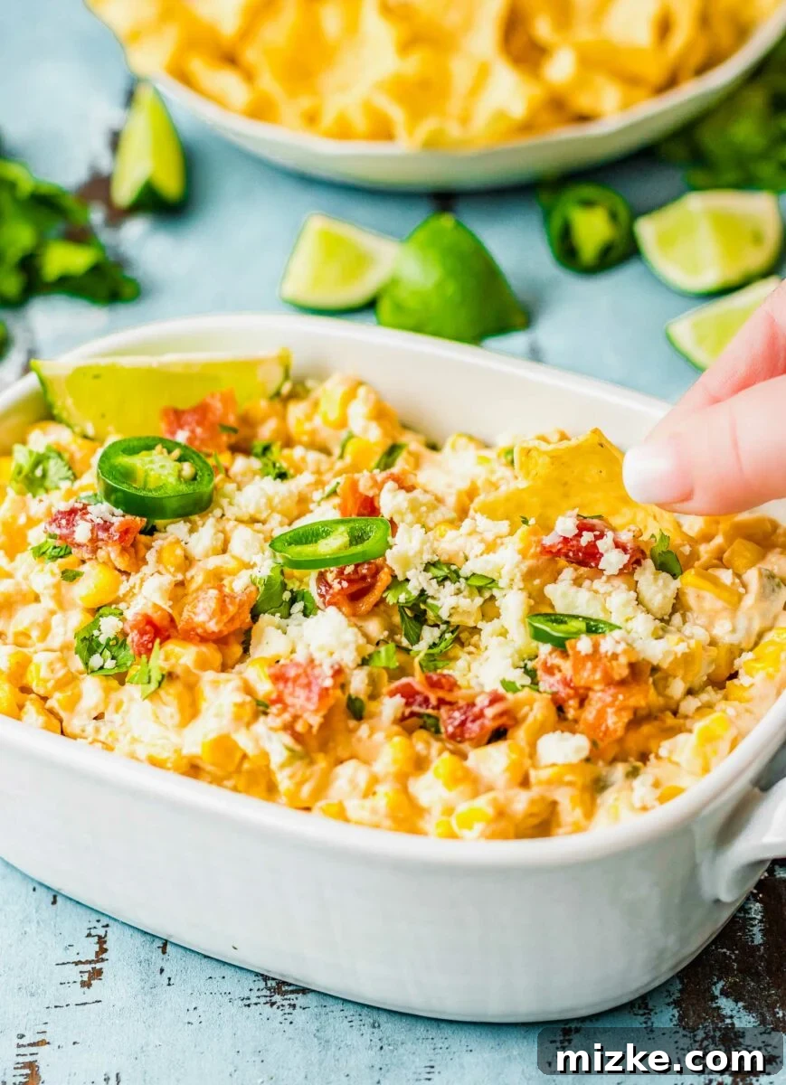 A chip is being dipped into warm, creamy jalapeño corn dip, showcasing its texture.