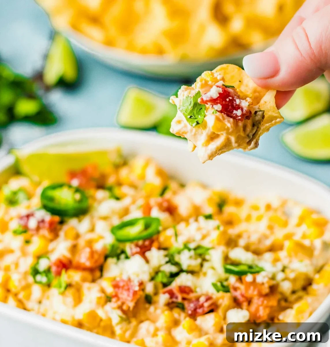 A chip has been dipped and has a good portion of creamy jalapeño corn dip on it, ready to be eaten.