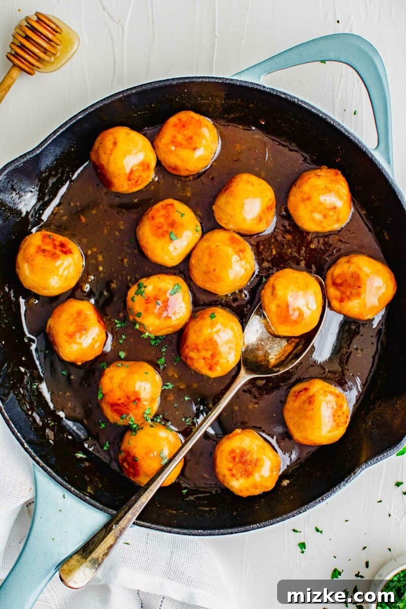 Fiery Honey Chicken Meatballs 2 A black skillet is filled with golden-brown chicken meatballs coated in a glistening hot honey sauce, ready to be served.