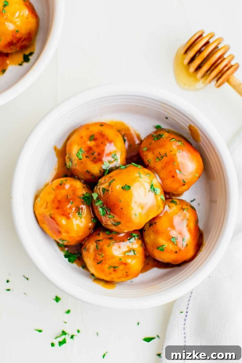Fiery Honey Chicken Meatballs 4 A crisp white bowl holds a generous serving of perfectly glazed hot honey chicken meatballs, garnished with fresh herbs.