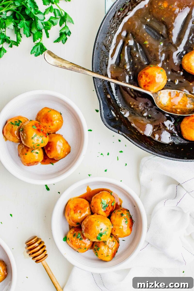 Fiery Honey Chicken Meatballs 5 Two white serving bowls filled with hot honey chicken meatballs are placed alongside a black skillet, indicating a fresh batch ready to be enjoyed.