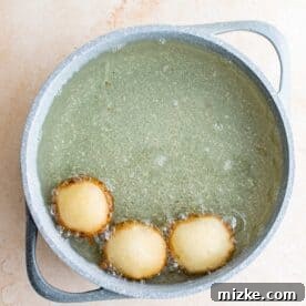 Three deep fried Oreos cooking in hot oil in a pot, turning golden brown.