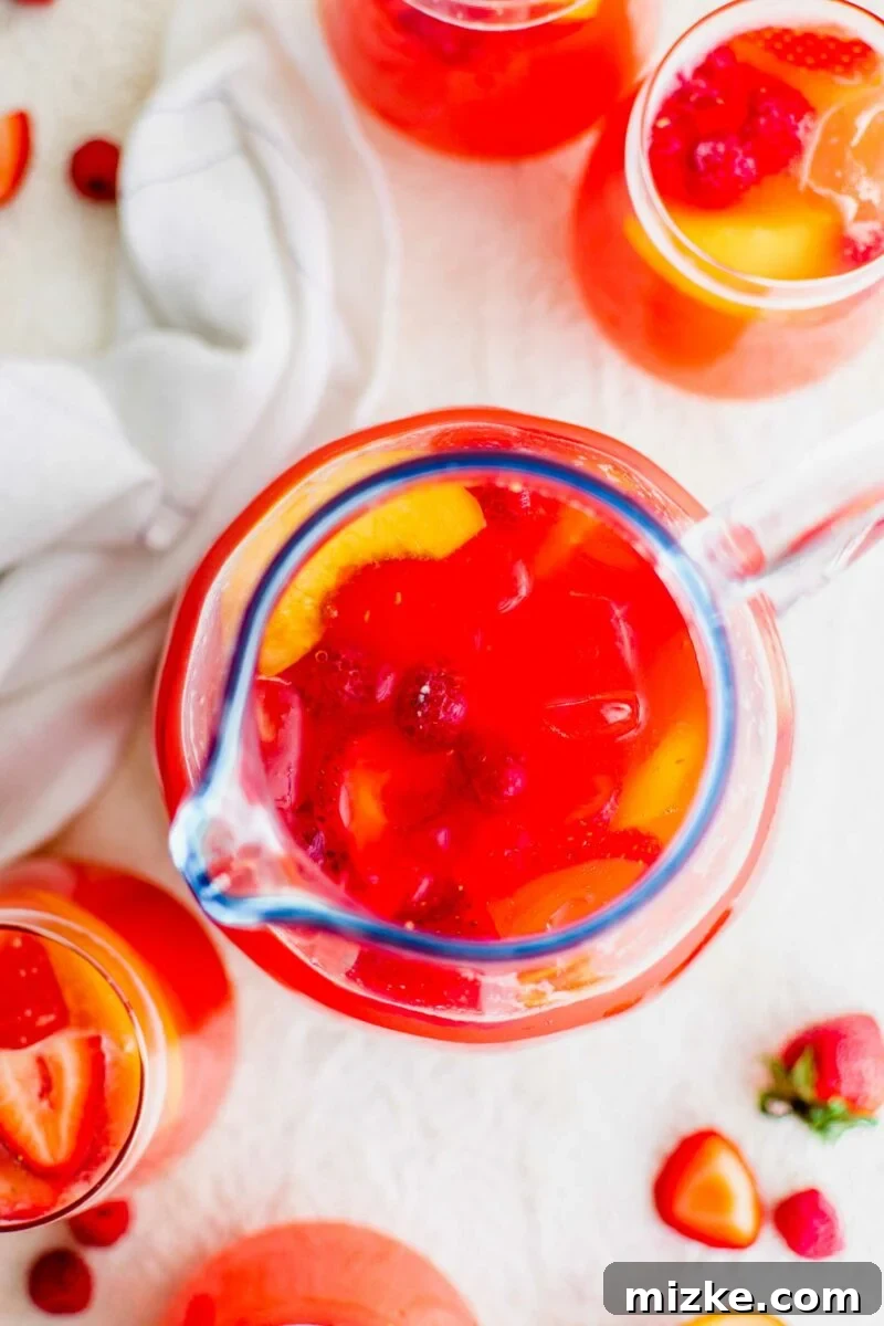 Cool Summer Delight 6 A pristine clear pitcher, filled to the brim with vibrant, refreshing summer punch, rests elegantly on a clean white surface.