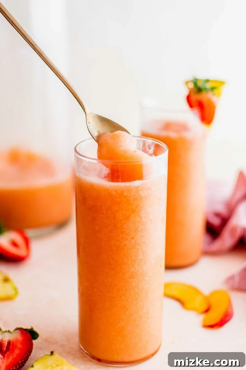 Summer's Spirited Slush 4 A spoon stirring a refreshing, multi-layered slushy drink in a tall glass, showcasing its icy texture and vibrant colors.