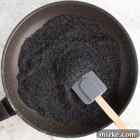 a large amount of black sesame seeds in a skillet with a silicone spatula