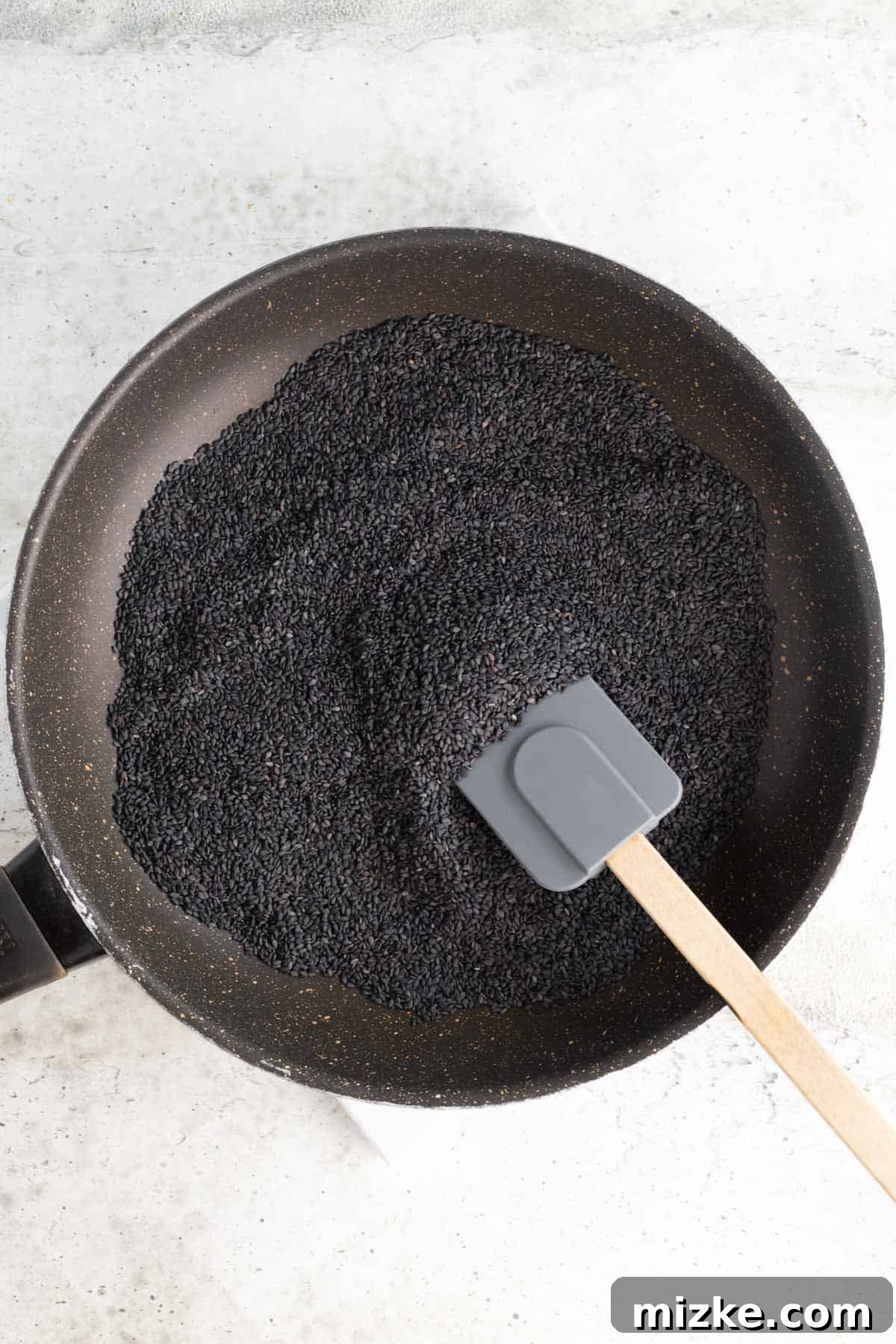 Midnight Sesame Dream 3 a large amount of black sesame seeds in a skillet with a silicone spatula