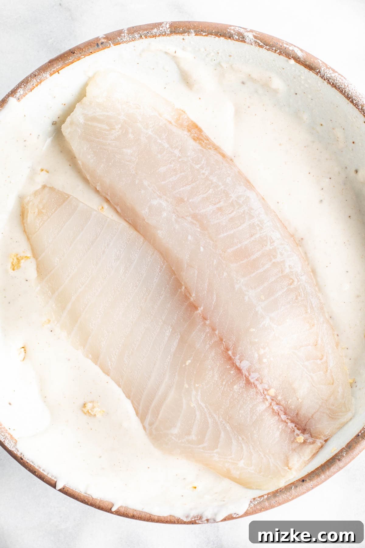 Southwestern Tilapia Crunch 5 A tilapia fillet is being carefully dipped into the seasoned liquid batter mixture.