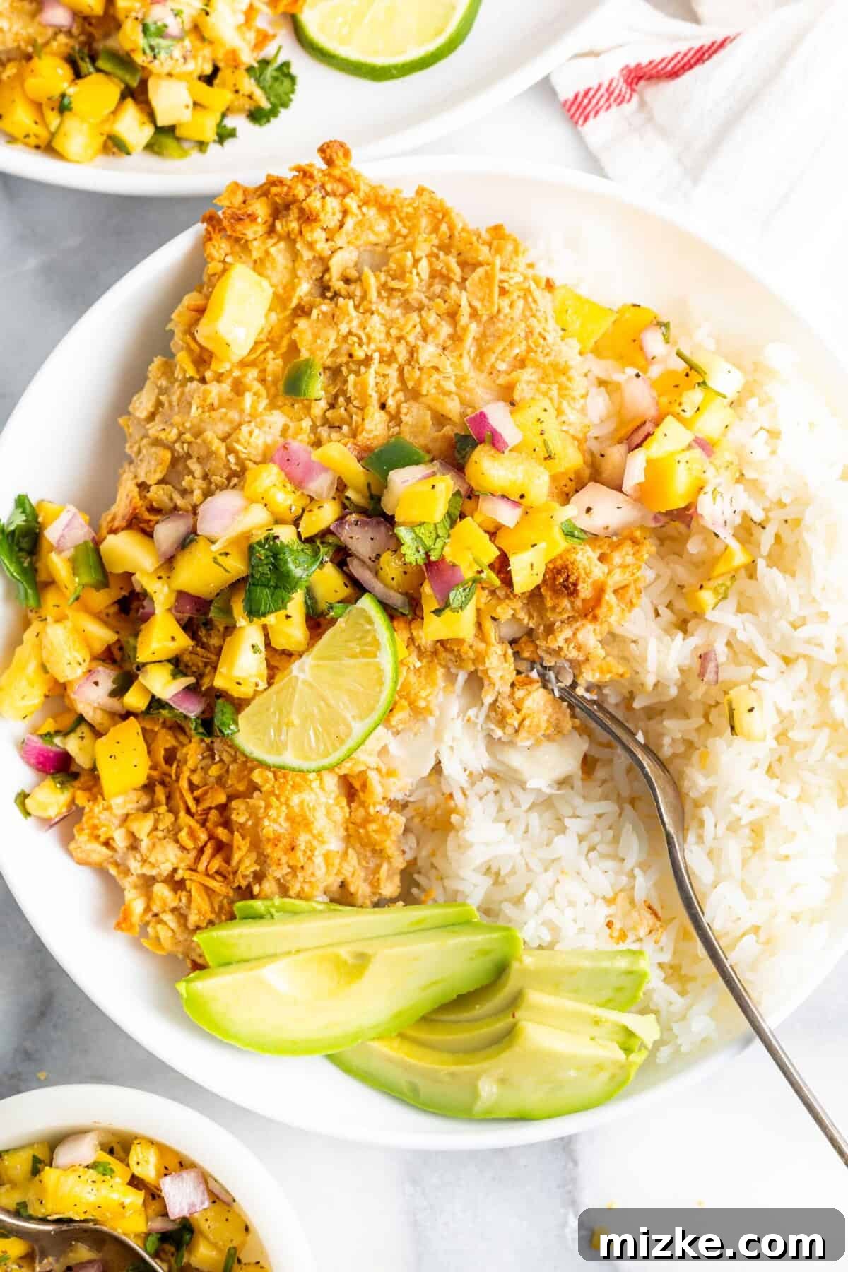 Southwestern Tilapia Crunch 7 A fork is placed in the center of a plate, removing a bite of tortilla crusted fish and rice, showcasing the crispy texture.