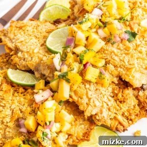 Baked tortilla crusted tilapia is garnished with limes and mango.
