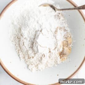 Flour, cornstarch, and seasonings in a shallow bowl with a metal spoon.