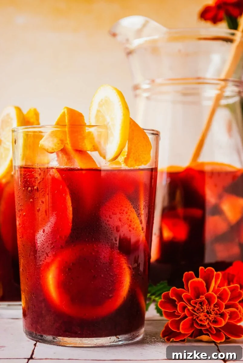 Orange flowers are placed on a tile surface next to a glass of sangria. 