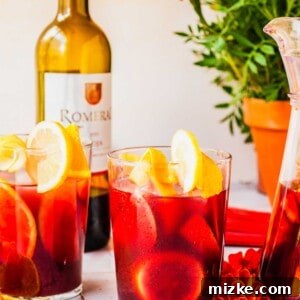 A glass pitcher and two glasses filled with Spanish Sangria and fresh fruit slices.