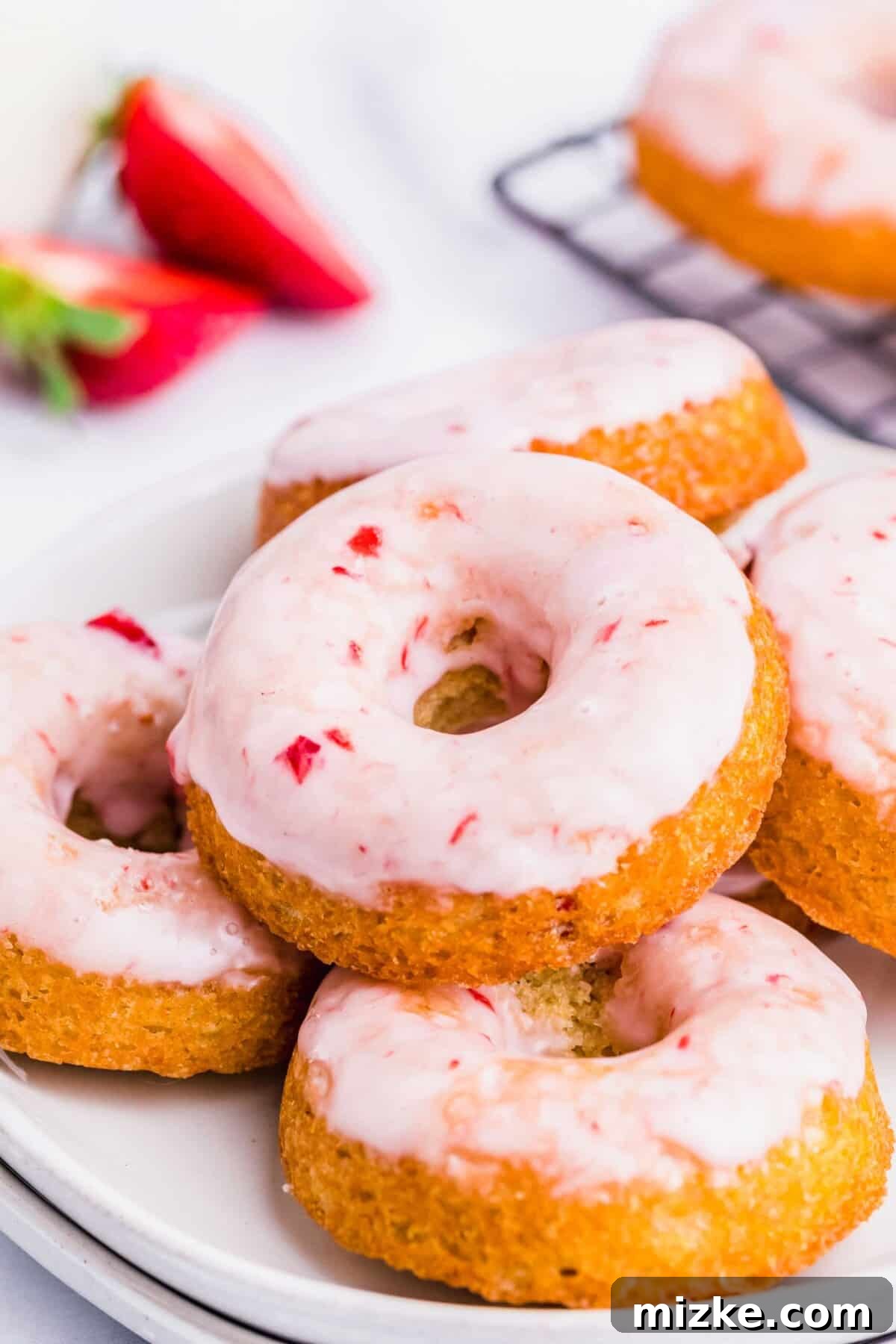Strawberry Oven Donuts 7 Several glazed strawberry donuts artfully arranged on a white serving platter, garnished with fresh whole strawberries.