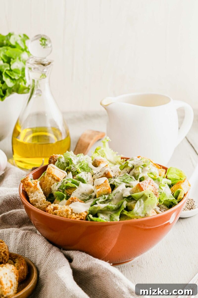 Plant-Based Caesar Salad 3 Olive oil is placed in a large glass jar behind a bowl of Caesar salad, showcasing fresh ingredients.