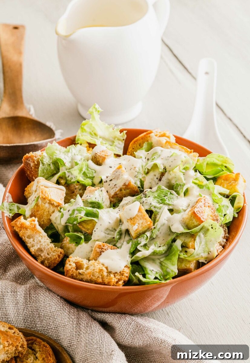 Plant-Based Caesar Salad 5 A bowl filled with salad is placed next to a tea cloth on a white surface, invitingly ready to be served.
