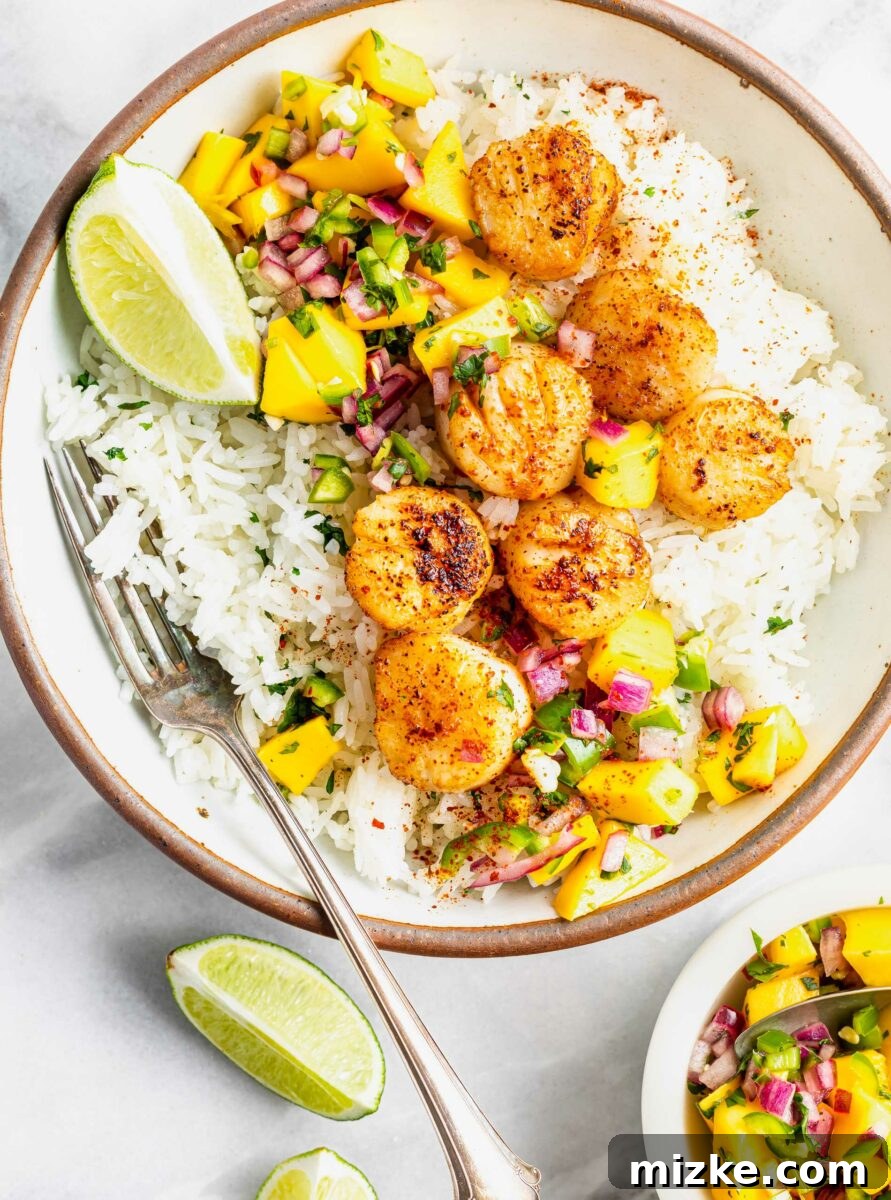 Seared Cajun Brown Butter Scallops 4 A fork gently rests in a bowl containing a blend of fluffy rice and perfectly cooked scallops, ready for tasting.