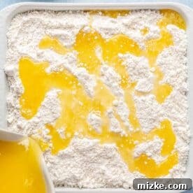 Melted butter is being carefully poured over the dry cake mix layer in the baking dish, which will help create the golden, crispy topping.