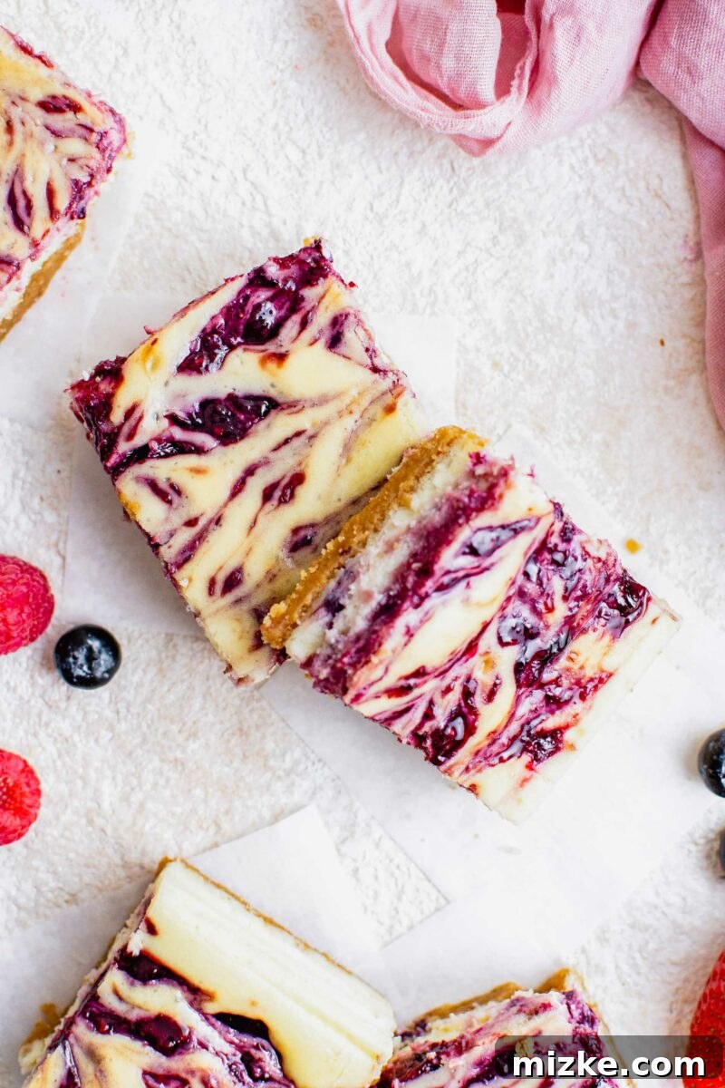 Vibrant Berry Cheesecake Squares 7 Several berry swirled cheesecake bars are placed together on a white surface, showcasing their inviting texture and colorful toppings.