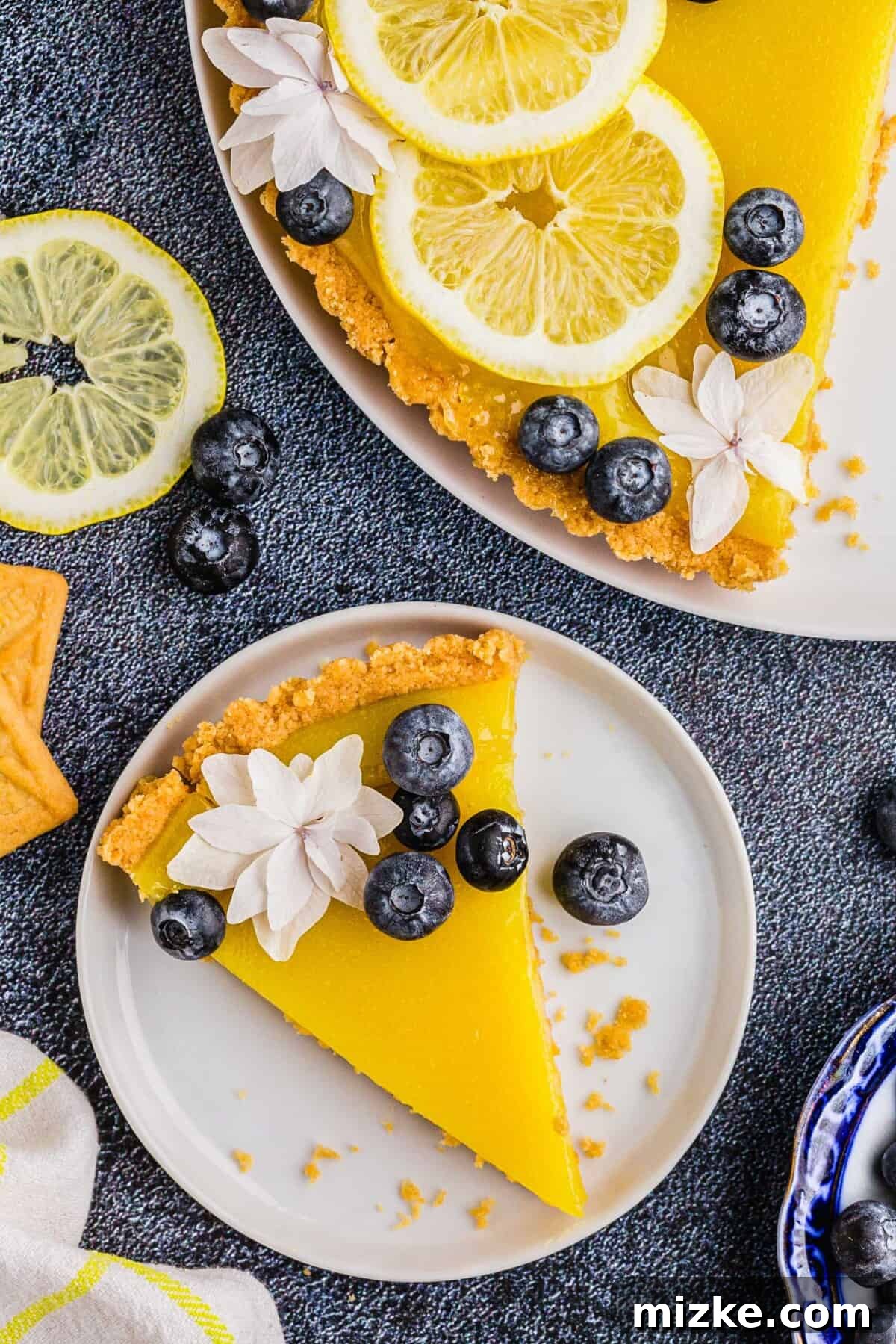 Bright Lemon Tart 11 A perfectly sliced piece of vibrant yellow lemon tart is elegantly presented on a pristine white plate, adorned with a scattering of fresh blueberries and a single delicate white flower, ready to be enjoyed as a gourmet dessert.