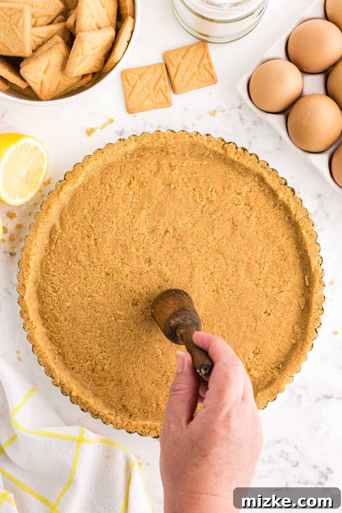 Bright Lemon Tart 7 Hands are shown firmly pressing the shortbread cookie crumbs into the bottom and gently up the sides of a metal tart pan, demonstrating the process of creating a smooth, compact, and perfectly formed crust.