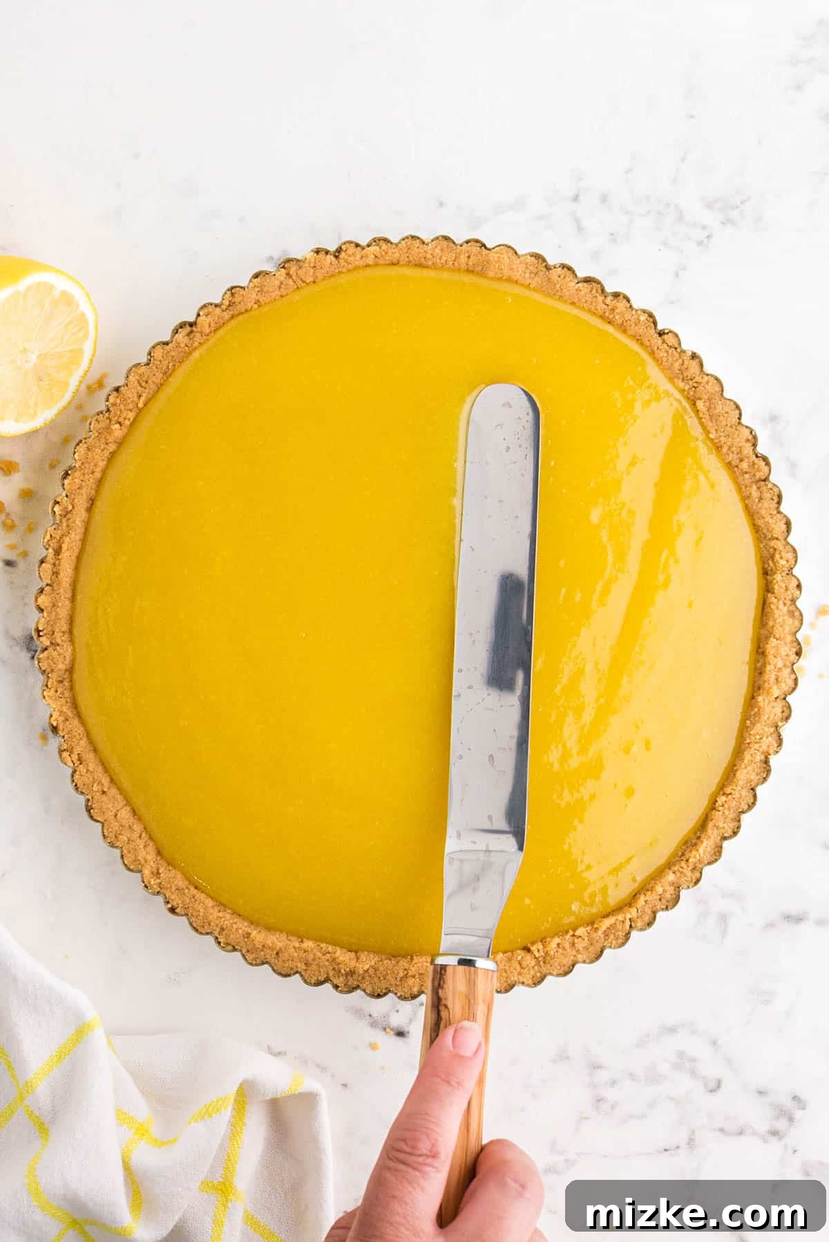 Bright Lemon Tart 9 An offset metal knife gently and expertly spreading a smooth, vibrant yellow lemon curd mixture evenly into the baked shortbread crust within a metal tart pan, creating a flawless surface.