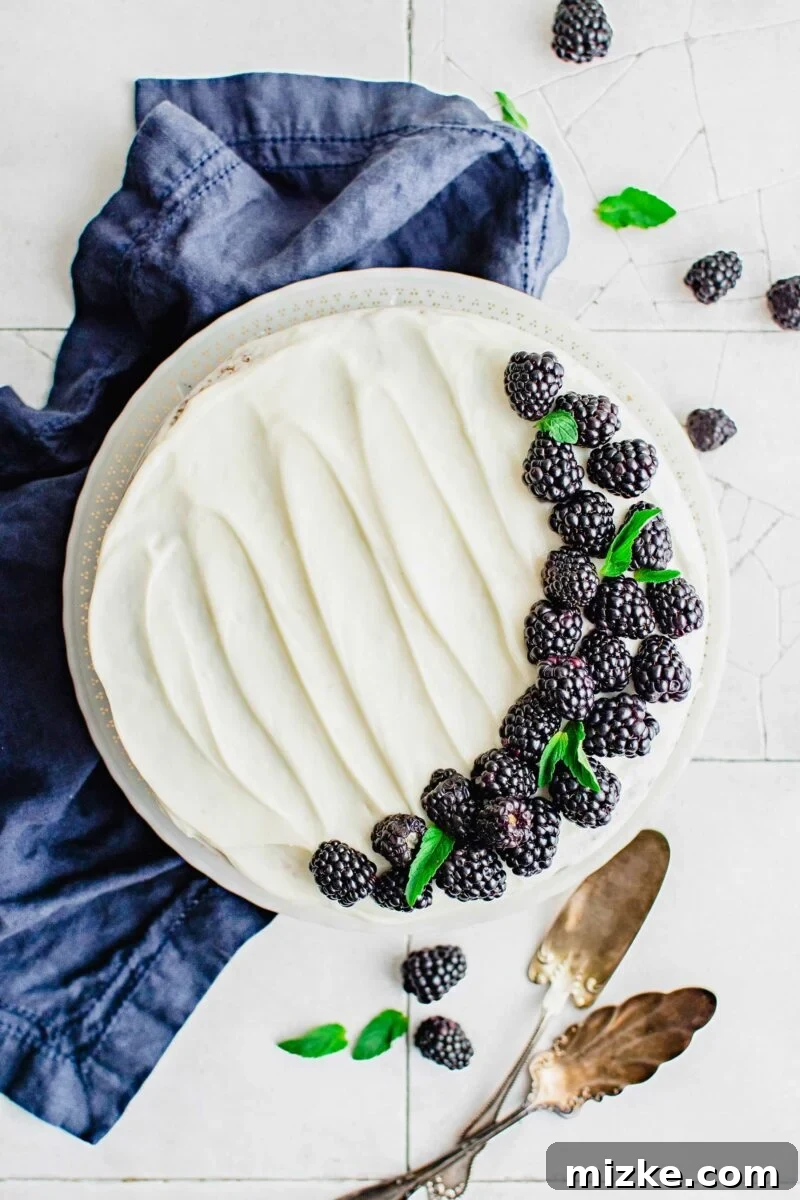 A beautifully frosted blackberry cake garnished with fresh blackberries, showcasing its vibrant purple hue and inviting texture.