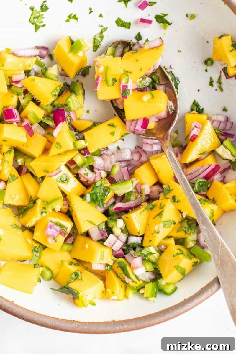 Sweet & Tangy Mango Burst 2 A spoon is scooping a small portion of bright orange and green mango relish from a white bowl, showcasing its fresh ingredients.