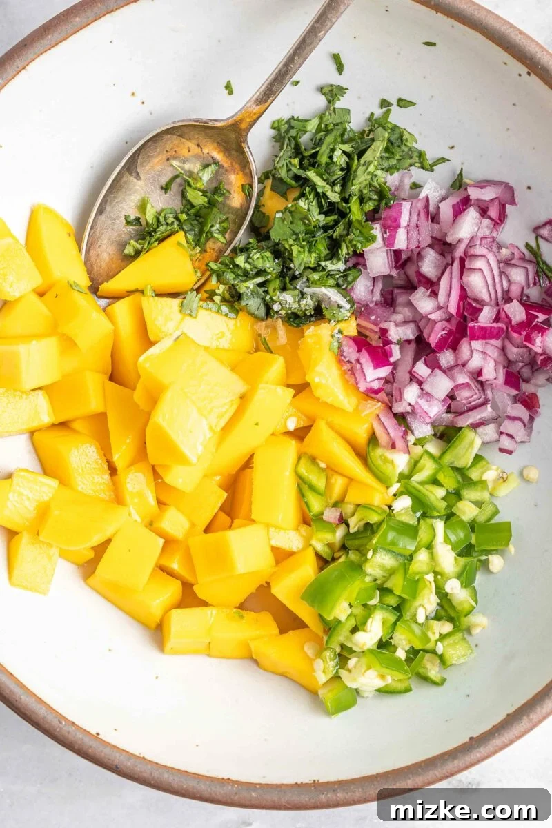 Sweet & Tangy Mango Burst 3 Diced mango, minced red onion, jalapeño, and fresh cilantro are unmixed in a small white bowl, ready to be combined for the relish.
