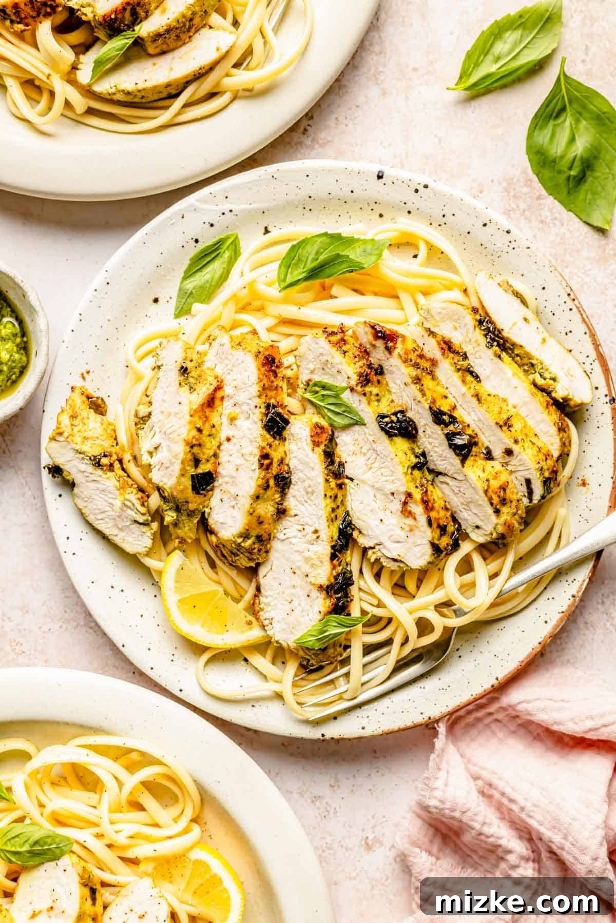 sliced lemon basil chicken on a plate of spaghetti noodles with a fresh lemon slice and fresh basil leaves