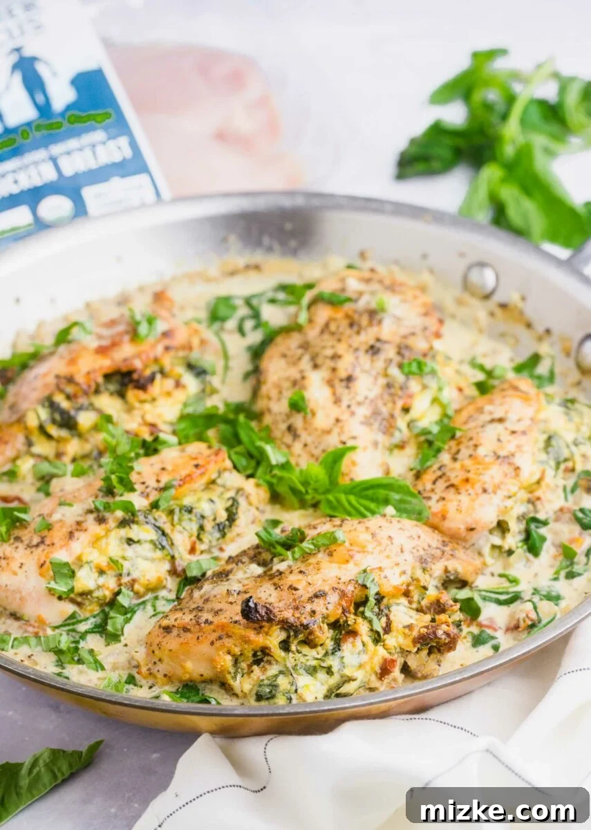 Sun-Kissed Tomato and Spinach Stuffed Chicken 2 A skillet is filled with golden-brown stuffed chicken breasts in a rich, creamy sauce, garnished with fresh herbs.