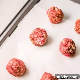 Steppe-Style Meatballs 6 Ground beef rolled into meatballs and neatly arranged on a baking sheet lined with parchment paper, awaiting oven baking.