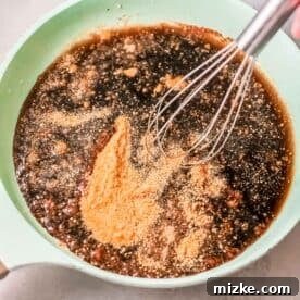 Steppe-Style Meatballs 7 Soy sauce, brown sugar, water, and other liquid ingredients being whisked in a green saucepan, forming the base of the sticky sauce.