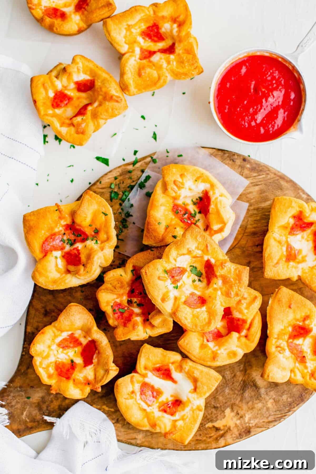 Portable Pizza Puffs 2 Golden brown pizza muffins arranged on a wooden cutting board, with a small bowl of pizza sauce nearby, hinting at the deliciousness within.