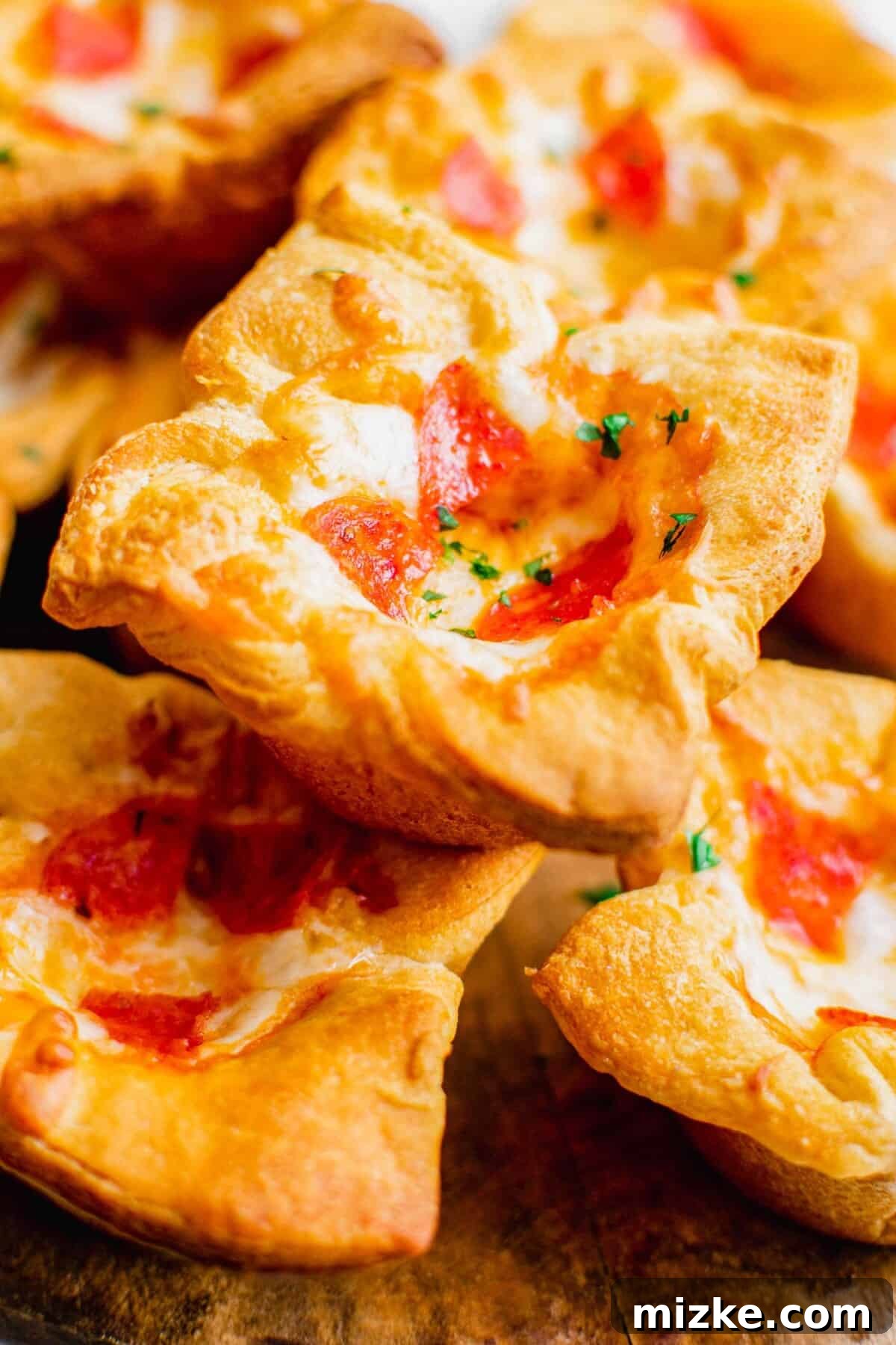 Portable Pizza Puffs 3 A perfectly baked pepperoni pizza muffin, garnished with fresh parsley, is stacked on top of several other golden-brown pizza muffins, showcasing their irresistible texture.