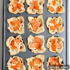 Portable Pizza Puffs 6 Crescent dough in muffin cups filled with robust pizza sauce, shredded mozzarella, and chopped pepperoni, ready for baking.