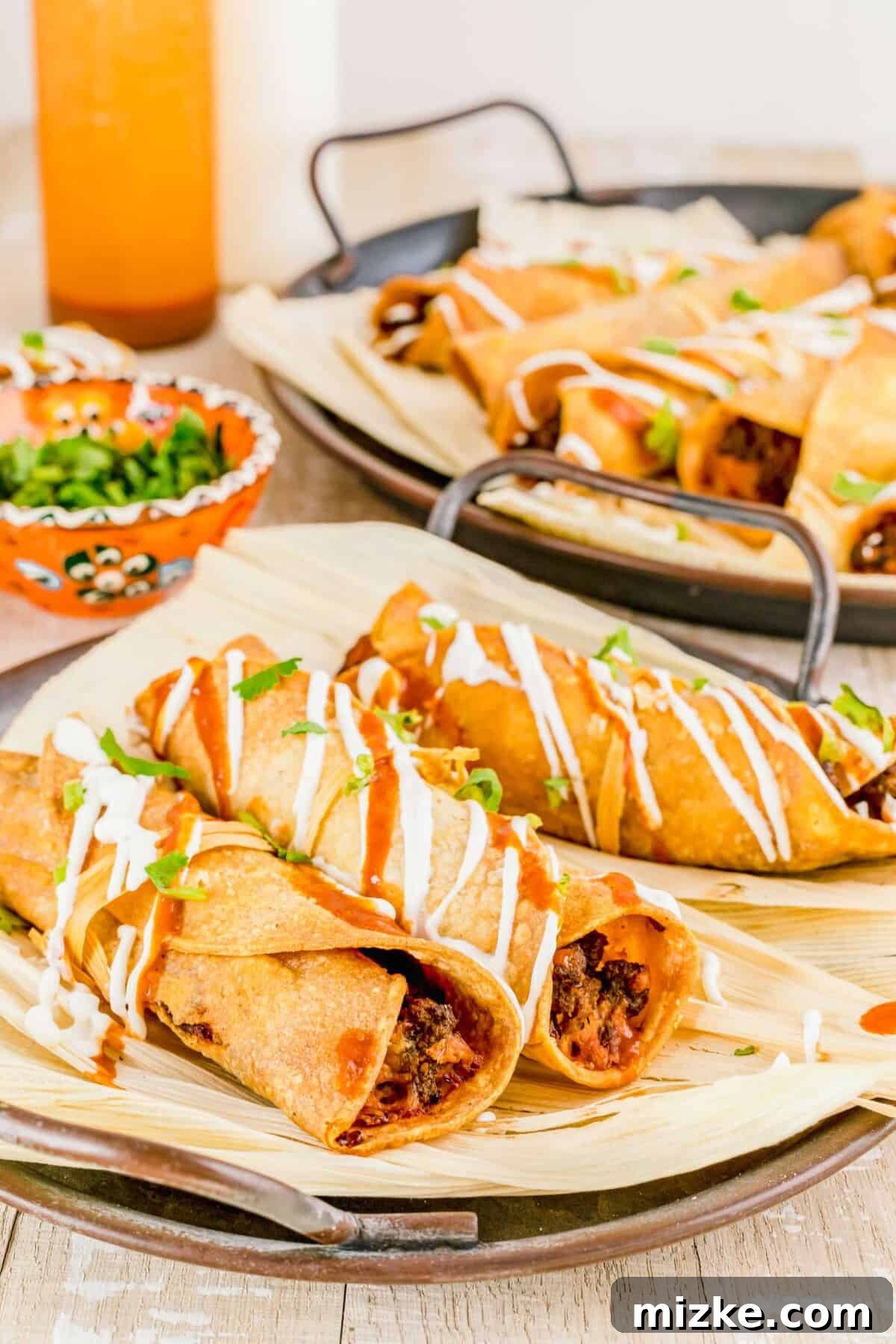 Crispy Air Fryer Beef Taquitos 11 Crispy air fried taquitos drizzled generously with sour cream and a red sauce, hinting at deliciousness.