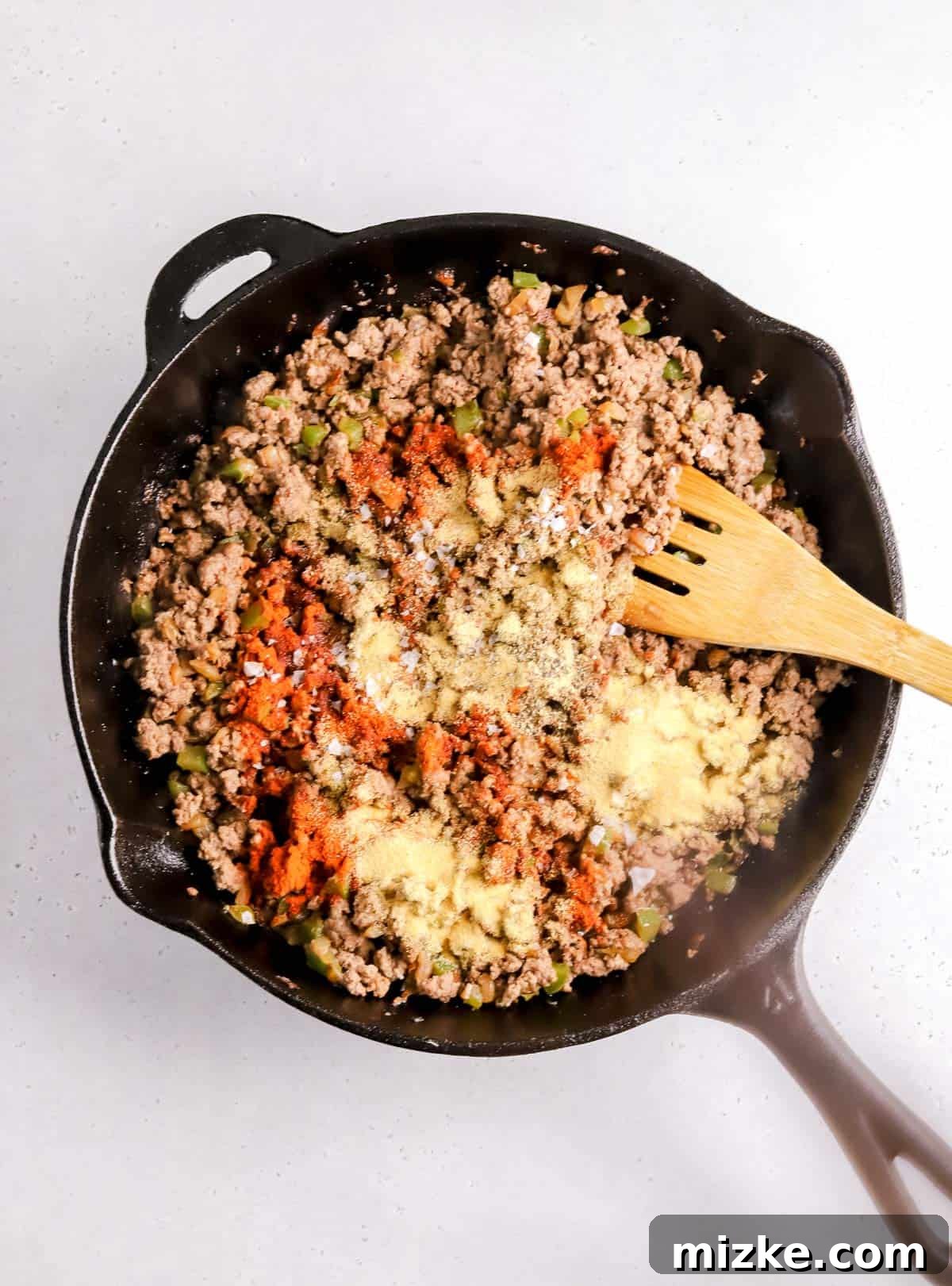 Crispy Air Fryer Beef Taquitos 5 Seasoned ground beef mixture with green bell peppers browning in a cast iron skillet, with spices sprinkled on top.