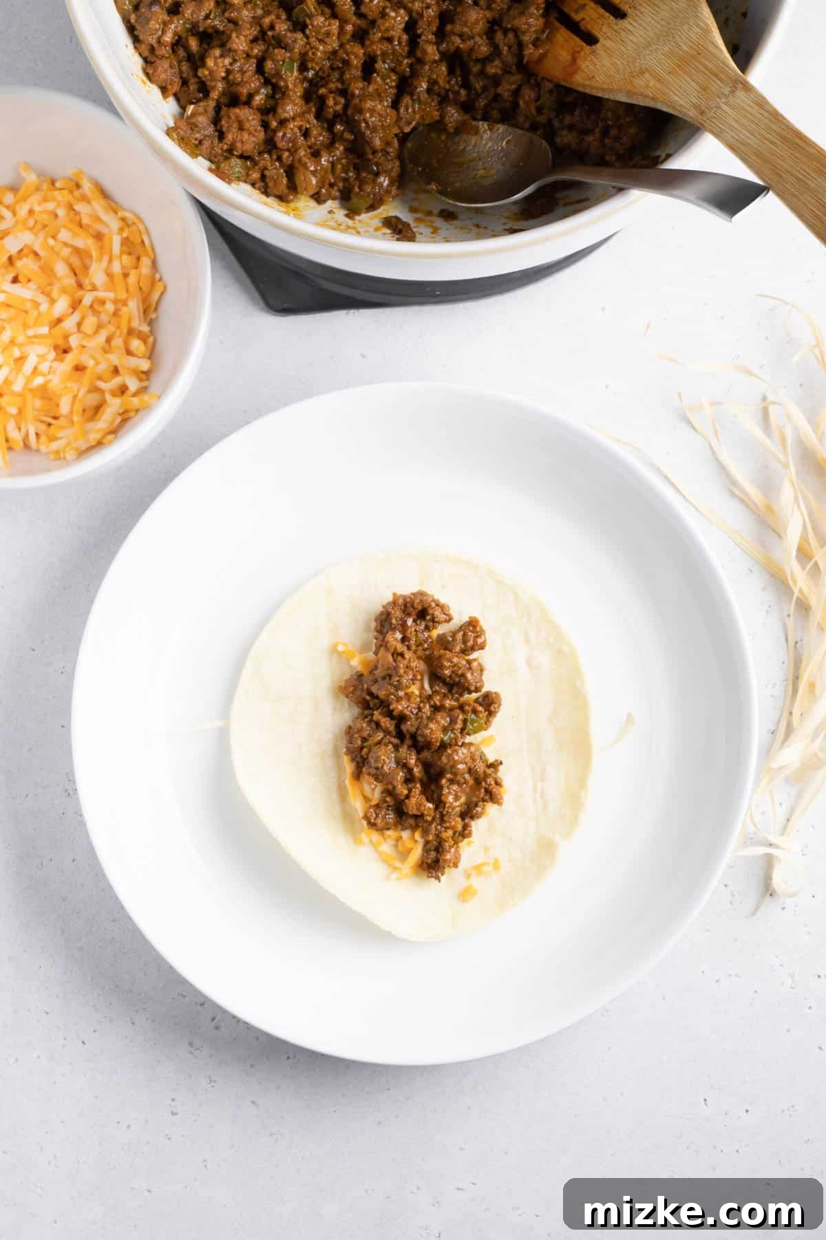 Crispy Air Fryer Beef Taquitos 7 Ground beef mixture layered on top of shredded cheese on a corn tortilla, ready for rolling, resting on a corn husk strip.