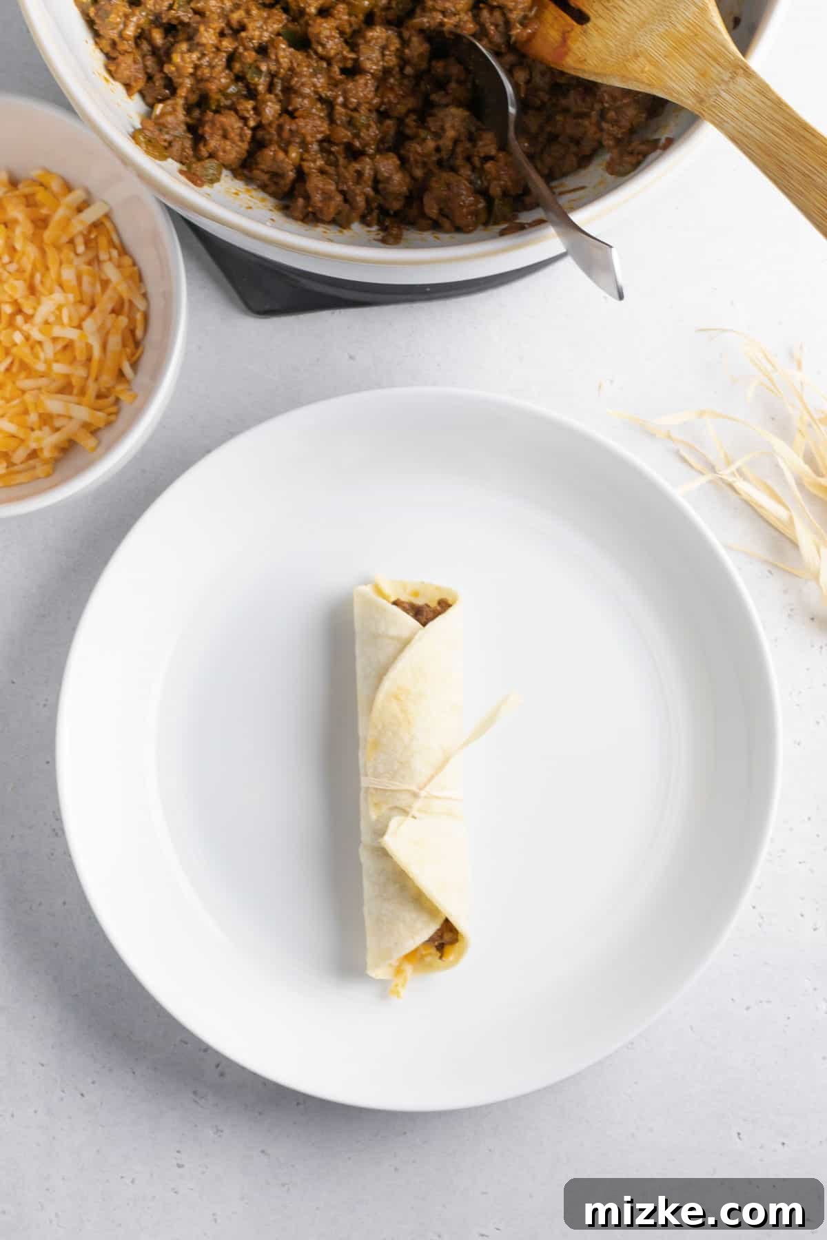 Crispy Air Fryer Beef Taquitos 8 A perfectly rolled beef taquito, tied securely with a corn husk strip, resting on a white plate.