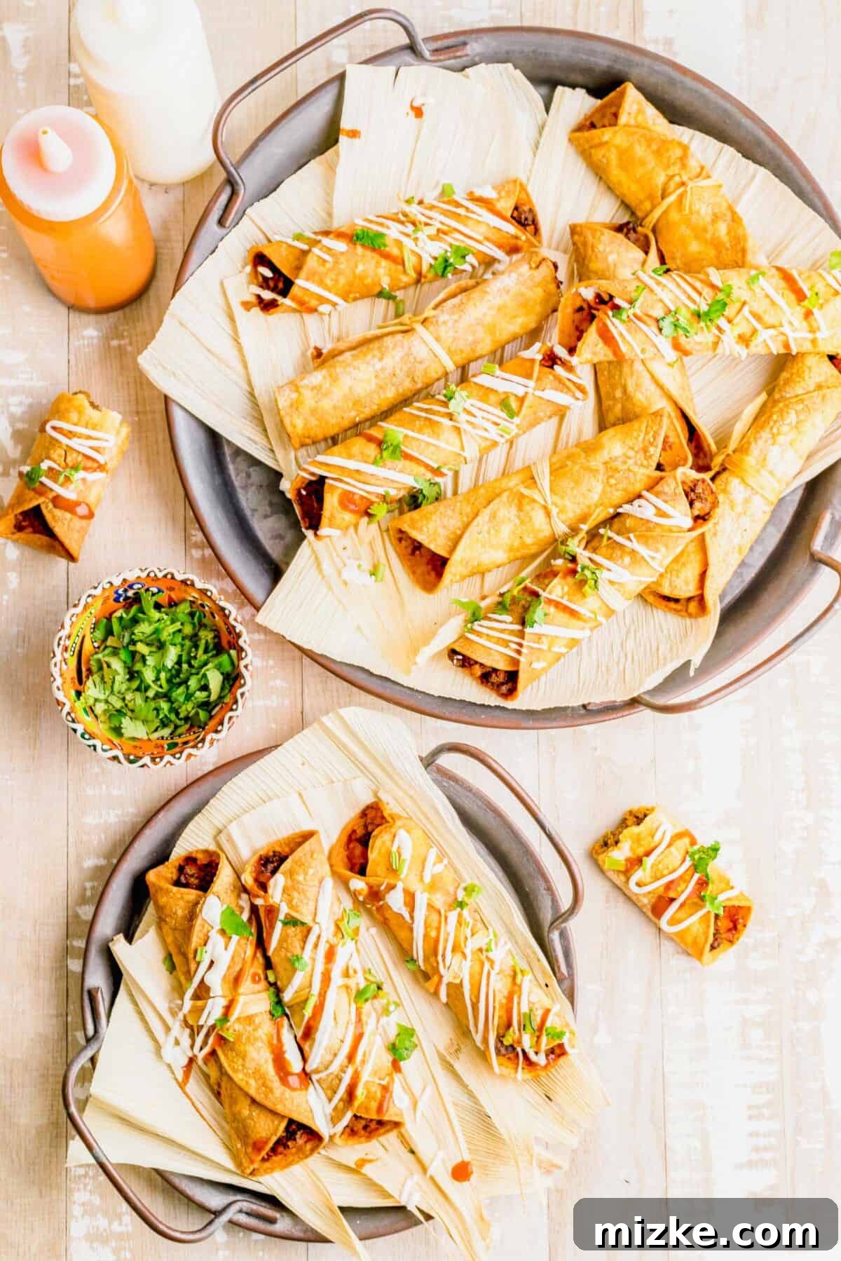 Crispy Air Fryer Beef Taquitos 10 Air fried beef taquitos arranged on corn husks, beside a small bowl of fresh cilantro for garnish.