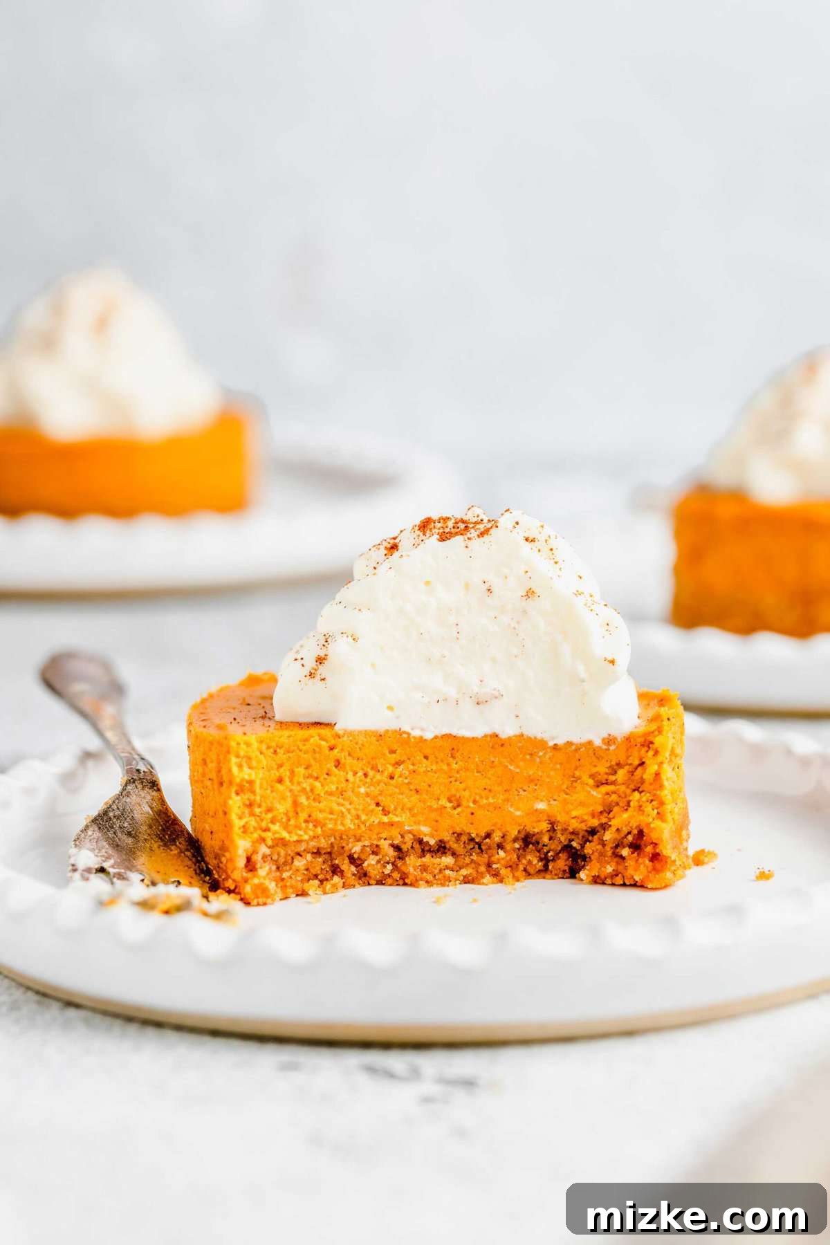 Creamy mini pumpkin cheesecake bites are the perfect crowd-friendly Thanksgiving dessert filled with mouthwatering pumpkin flavor. A mini pumpkin cheesecake bite on a plate, with a bite taken out of it and a fork on the plate, with two cheesecake bites on plates in the background