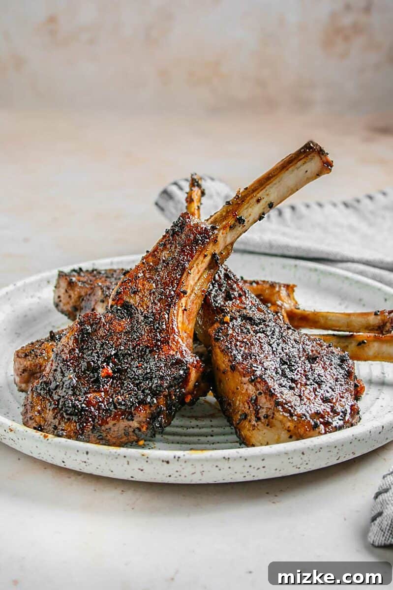 Smoky Coffee Rubbed Grilled Lamb Chops 2 Several grilled lamb chops are presented on a spotted white plate, garnished with fresh herbs.